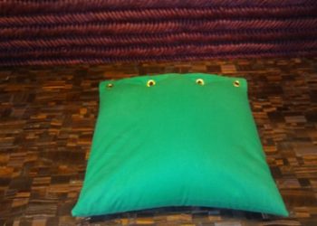 A green pillow sitting on top of a wooden floor.