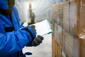 A person in blue jacket holding clipboard near boxes.